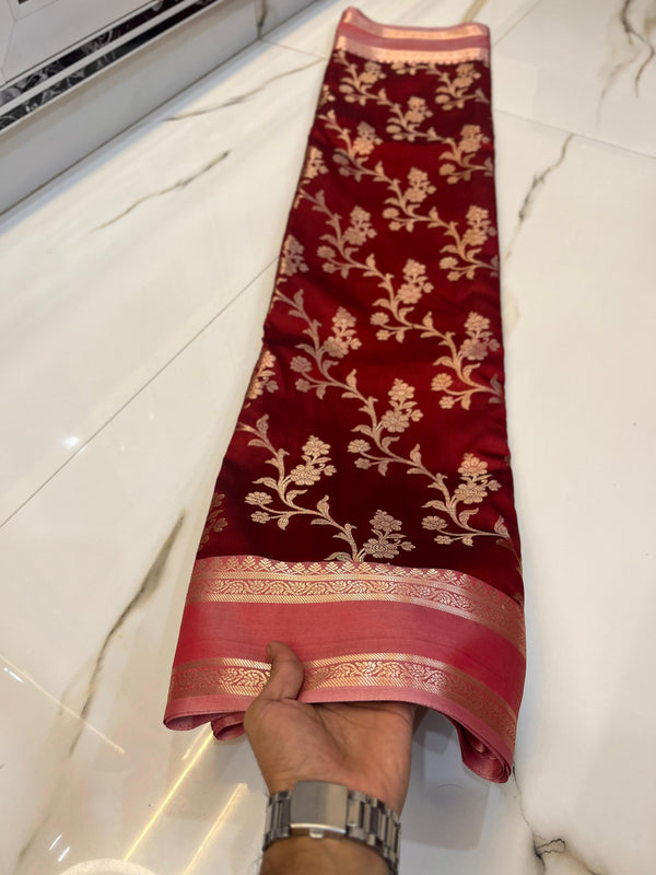 Red saree with floral patterns held by a hand on a white floor.