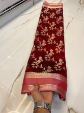 Red saree with floral patterns held by a hand on a white floor.